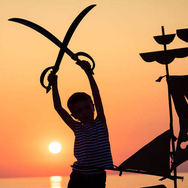 Enfant avec des épées pirates devant un coucher de soleil