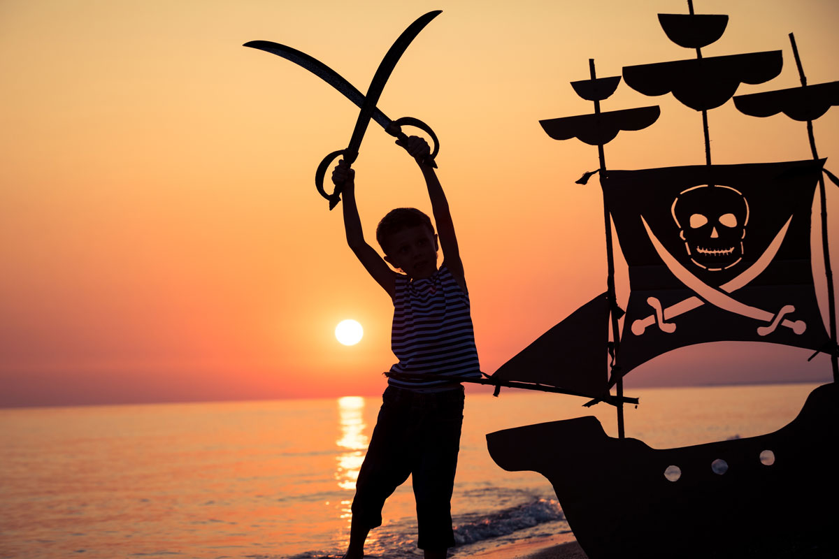 Enfant avec des épées pirates devant un coucher de soleil